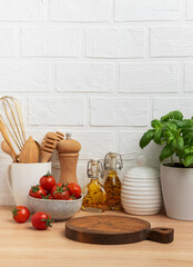 Kitchen countertop with cutting board, tomatoes, spices, and basil plant
