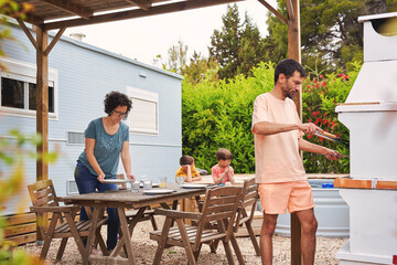 Family preparing meal outdoors near caravan and pool in summer