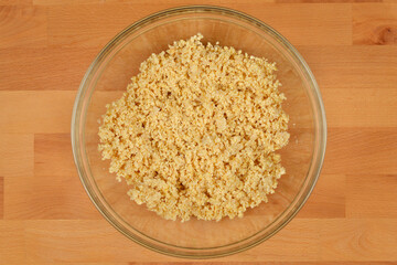 A clear glass bowl contains a pile of processed, light yellow ground soybeans on a light brown wooden surface