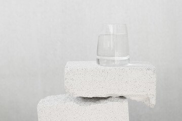 Balancing composition with stone blocks and glass with pure water on a neutral background