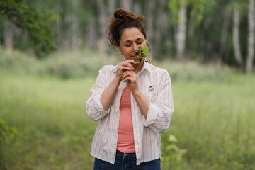 Woman enjoying simple pleasure of fresh wild strawberry aroma in summer forest. Female relaxing outdoors feeling calmness and connection with nature