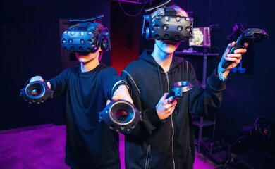 Cooperation, standing together. Two young men in virtual reality glasses indoors