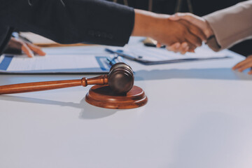 Two businesspeople are shaking hands in a law office with a scale and a gavel on the table.