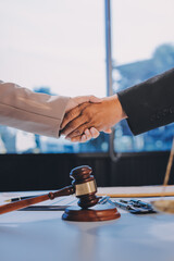 Two businesspeople are shaking hands in a law office with a scale and a gavel on the table.