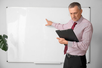 Male teacher with clipboard pointing at flipboard in classroom