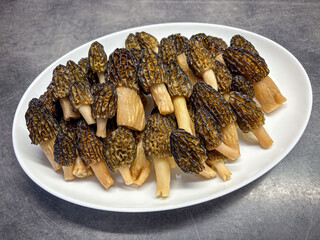 White plate with edible morel mushrooms on gray table