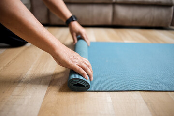 Side view of a person rolling up a blue mat at floor, preparing for yoga practice