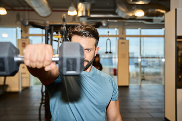 Focused man lifting dumbbell in modern gym