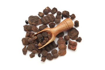 A wooden scoop filled with organic Shikakai (Acacia concinna), placed on a heap of shikakai fruits, isolated on a white background.