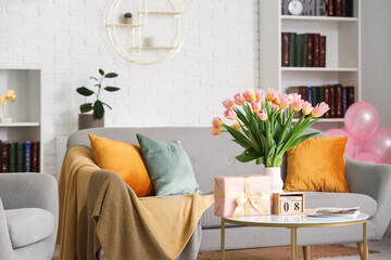 Calendar with date of International Women's Day, tulips and gift box on table in living room