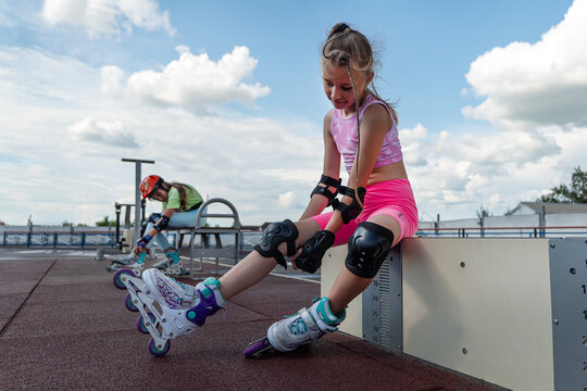 Young skater girl putting on protective shin guards and knee pads for skating. children female rollerblader preparing for a ride in skatepark in summer