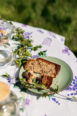 A rustic outdoor table setting featuring a homemade slice of bread on a green plate, surrounded by greenery and glass jars. Perfect for food photography, lifestyle branding, and rustic themes.