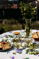 A rustic table set outdoors with glass jars, a vase of greenery, bread slices on a floral plate, and a hand holding a glass teacup. Perfect for garden dining, lifestyle branding, and food photography