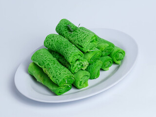 Traditional Indonesian dadar gulung, a sweet coconut-filled green crepe served on banana leaf. Authentic jajanan pasar (market snack) with rustic presentation.