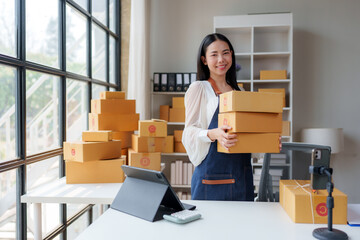 Asian female seller holding parcel boxes in a startup office, managing sme business with online...