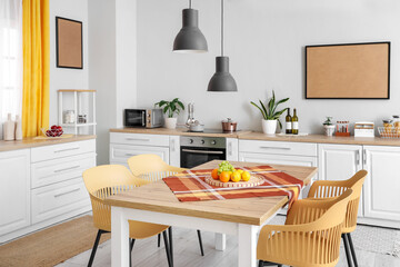 Interior of beautiful kitchen with white counters, dining table, fruits, chairs and lamps