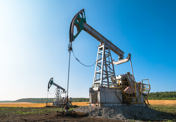 Oil pumps operate in a vast field under a clear blue sky at midday in rural area