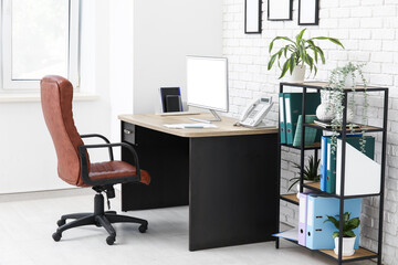 Interior of stylish office with workplace, armchair, modern computer and shelving unit