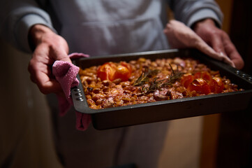 A freshly prepared baked dish featuring tomatoes and herbs, held in a black tray. Showcasing vibrant textures and colors, this scene represents homemade cooking and warm culinary traditions.
