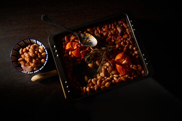 Delicious baked beans with roasted tomatoes and fresh rosemary showcased in a rustic, contrasting...