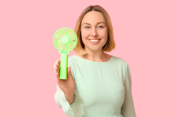 Beautiful mature happy woman with mini green electric fan on pink background