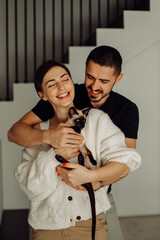 Happy couple holding siamese cat and smiling at home