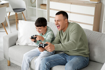 Cute little boy with his father playing video game on sofa at home