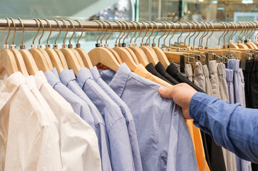 Man chooses a male shirt hanging on hanger in store, side view.