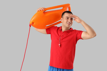 Happy male lifeguard with life board looking at something on grey background