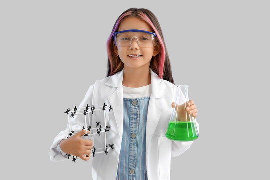 Cute little girl with chemistry flask and molecular model on grey background