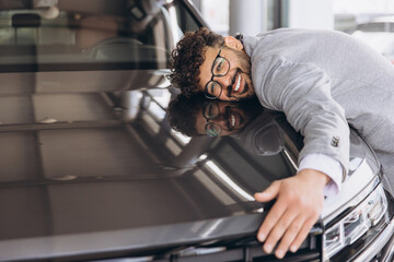 Smiling man hugging a car in a modern showroom