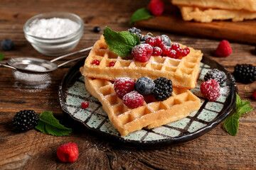 Plate of sweet Belgian waffles with different fresh berries and mint on wooden background