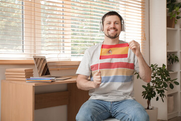 Handsome man in headphones with flag of Spain learning language online at home