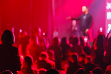 Blurred silhouette of audience at live event under intense red lighting creating energetic...