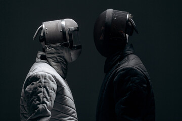 Two Fencers Facing Each Other in Protective Gear on a Moody Dark Background..