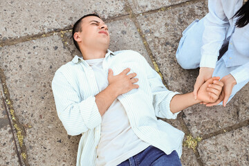 Young woman checking pulse of her husband having heart attack on street, top view
