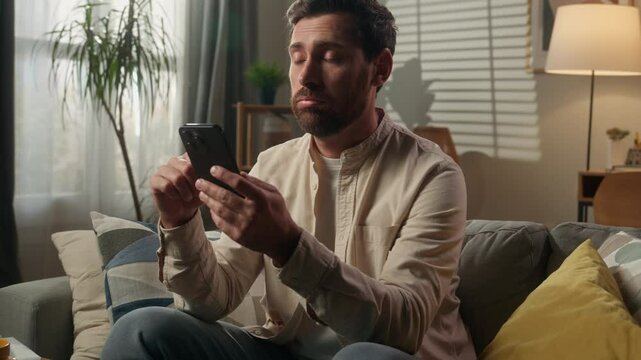 Frustrated sad Caucasian man homeowner businessman upset disappointed male guy browsing mobile phone internet on home couch sofa smartphone receive message bad news worried scam failure in living room