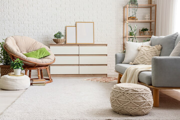 Comfortable sofa, armchair, chest of drawers, shelving unit and poufs in interior of living room