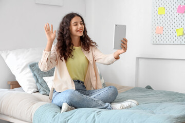 Teenage girl with tablet computer video chatting in bedroom