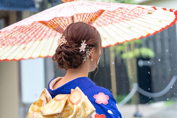 Fototapeta premium A local city in Japan on a rainy summer day. A Japanese woman wearing a blue teenage kimono holding a Japanese umbrella and climbing a slope. The back view.