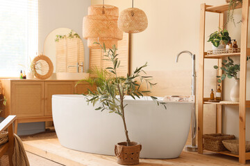 Interior of comfortable bathroom with chest of drawers, bathtub, houseplant and lamp