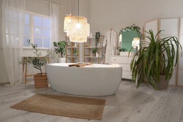 Interior of bathroom with bathtub, plants and glowing lamps in evening