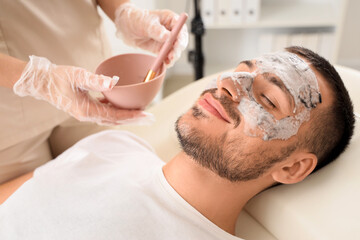 Beautician applying cosmetic bubble mask on handsome man's face in spa salon