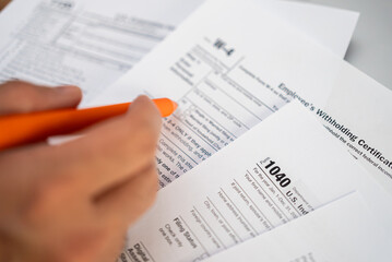 Fototapeta premium Male freelancer hand holds pen preparing for filling necessary tax forms to report annual income to comply with federal and state tax laws avoiding penalties
