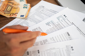 Naklejka premium Male freelancer hand holds pen preparing for filling tax forms keeping detailed records of income and expenses sitting at workplace with euro banknotes