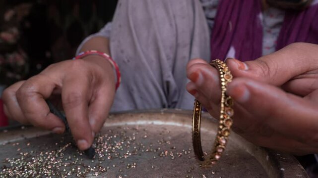 A close-up of a hand putting diamonds to bangles 
