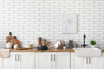 Sink, houseplants and utensils on counter near white brick wall in kitchen