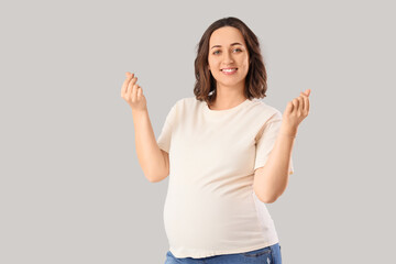 Young pregnant woman making heart gesture on light background. Rules concept