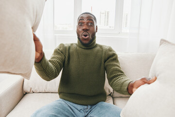 Excited Black man with pillows enjoying cozy indoor moments in a green sweater, expressing joy and...