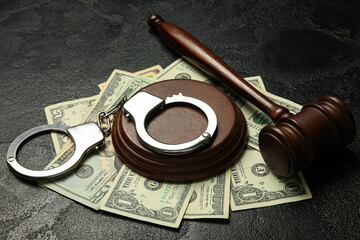 Handcuffs with judge's gavel and dollar banknotes on dark background, closeup